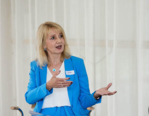 Gina Nauen spricht mit offener Gestik bei einem Business-Event – Beispiel für Präsenz und Ausstrahlung durch Stimme und Körpersprache